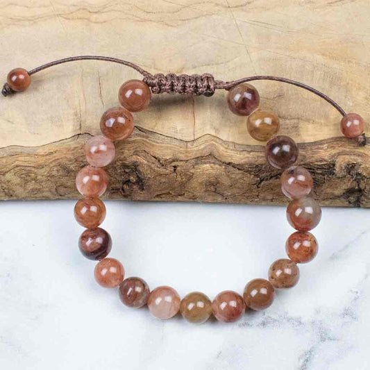 A bracelet with a series of round beads in various shades of brown, beige, and white, displayed on a wooden surface.