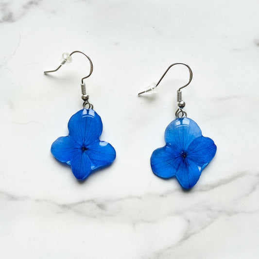 Handmade pressed hydrangea flower earrings in clear resin with sterling silver hooks, displayed on a neutral background.
