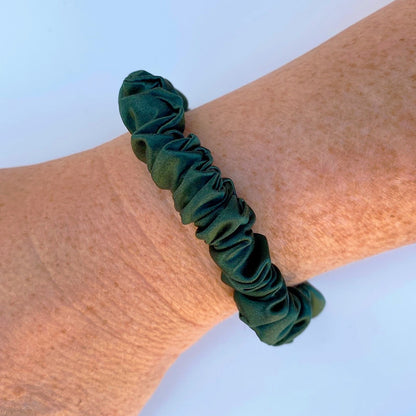 Forest green silk scrunchie on a wrist against a light blue background