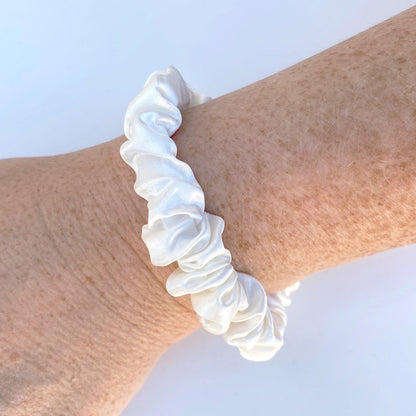 White silk scrunchie scrunchie on a wrist against a light blue background