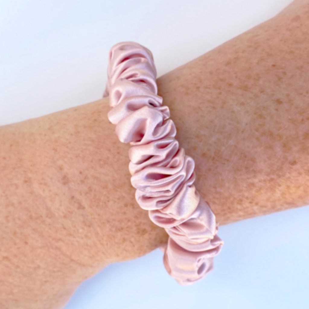 Pale pink silk scrunchie on a wrist with a light background