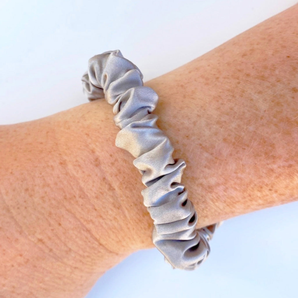 Silver silk scrunchie on a wrist against a light blue background