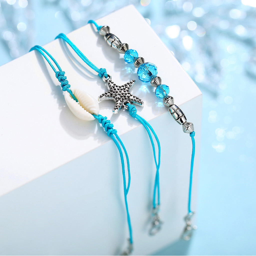 Three-piece bohemian beach anklet set featuring teal wax rope, a natural seashell, a starfish charm, and blue beads.