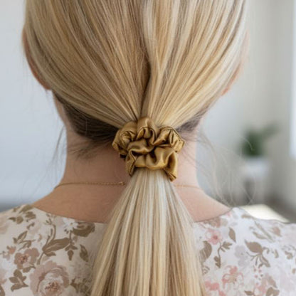 Person with blonde hair tied in a ponytail using a gold silk scrunchie, wearing a floral top.